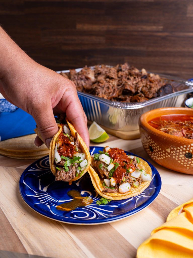 Table with tacos and ingredients and a hand reaching in to grab a taco