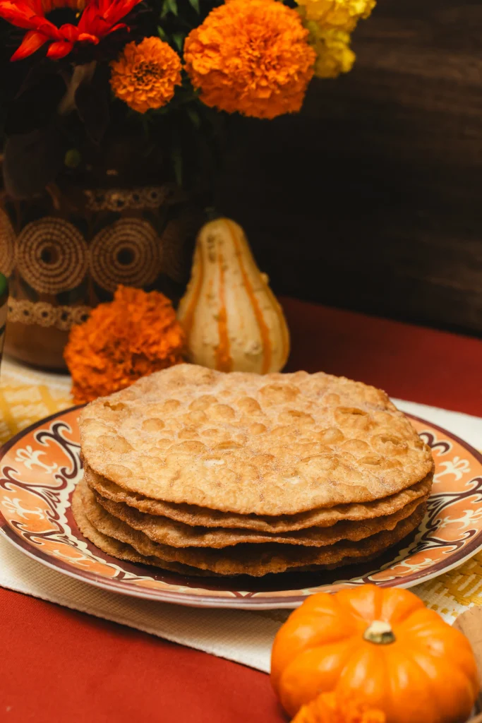 Stack of traditional buñuelos on a decorative plate, surrounded by marigolds and fall decorations.