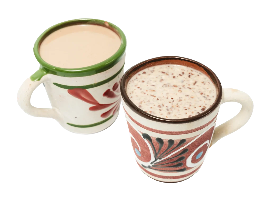 Two mugs of traditional Mexican drinks, one filled with champurrado and the other with atole, served in hand-painted clay mugs.