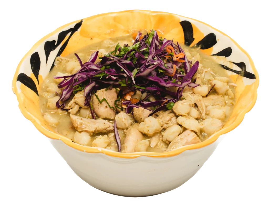 Bowl of green pozole topped with shredded chicken, hominy, and garnished with purple cabbage and herbs.