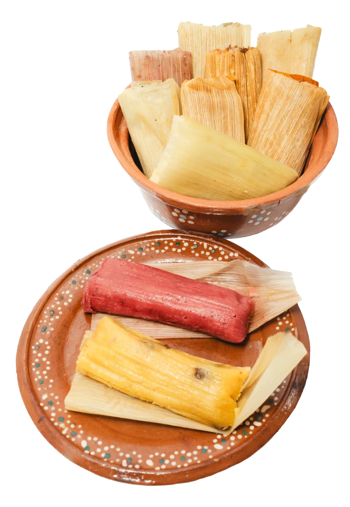 Assorted tamales wrapped in corn husks, served on traditional Mexican clay plates.