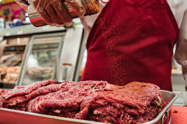 Northgate Market butcher seasoning raw beef in a tray.