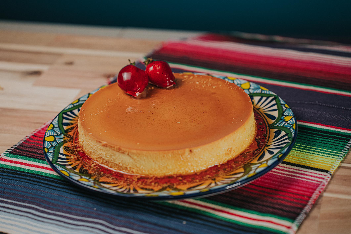Beauty shot of flan on a plate with strawberries on top.