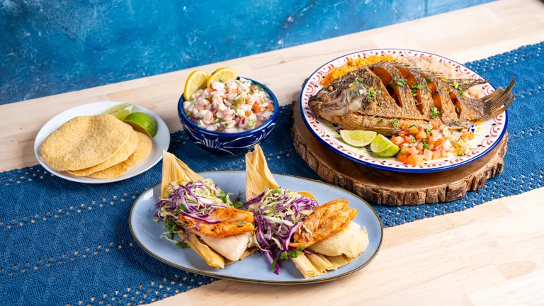 Grilled whole fish with lime and pico de gallo, shrimp and fish tamales topped with cabbage slaw, and a bowl of ceviche with tostadas and lime wedges