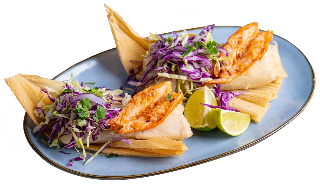 Shrimp tamales topped with red and green cabbage slaw and served with lime wedges