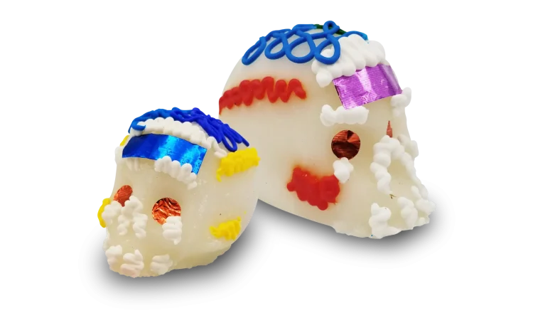 Two traditional Mexican sugar skulls decorated with colorful icing and metallic foil accents.